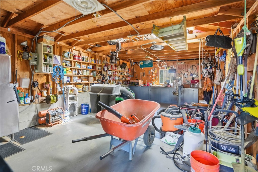 Workshop with exposed wooden beams, tool-filled shelves, a workbench, and a red wheelbarrow.