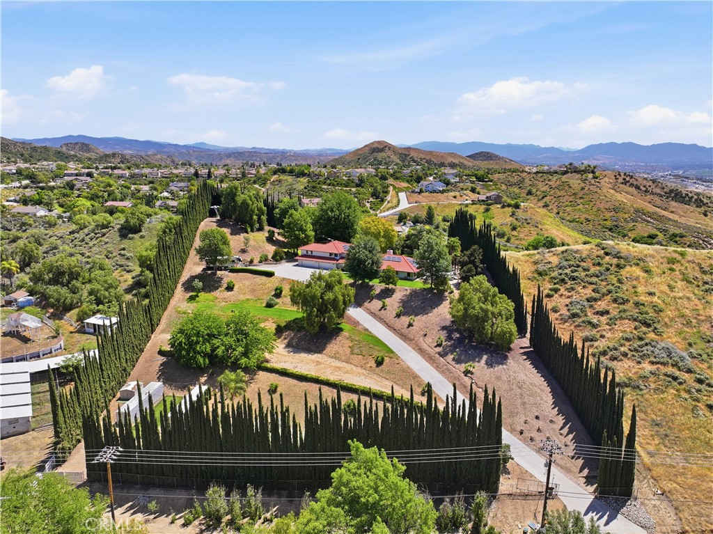 Aerial view of a home bordered by tall cypress trees, with hills and mountains beyond.