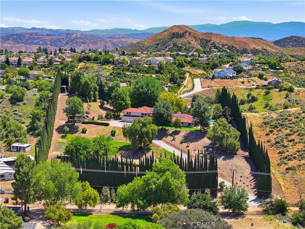 Aerial view of a hillside home with cypress-lined grounds and mountains beyond.
