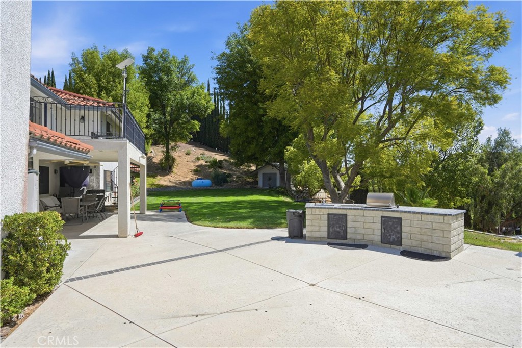 Backyard patio with a built-in stone grill, covered dining area, and lawn beneath mature trees.