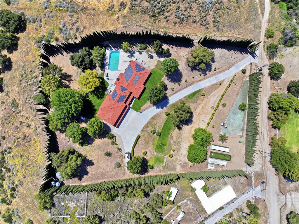 Aerial view of a red-tile-roof home with solar panels, swimming pool, lawn, and curved driveway.