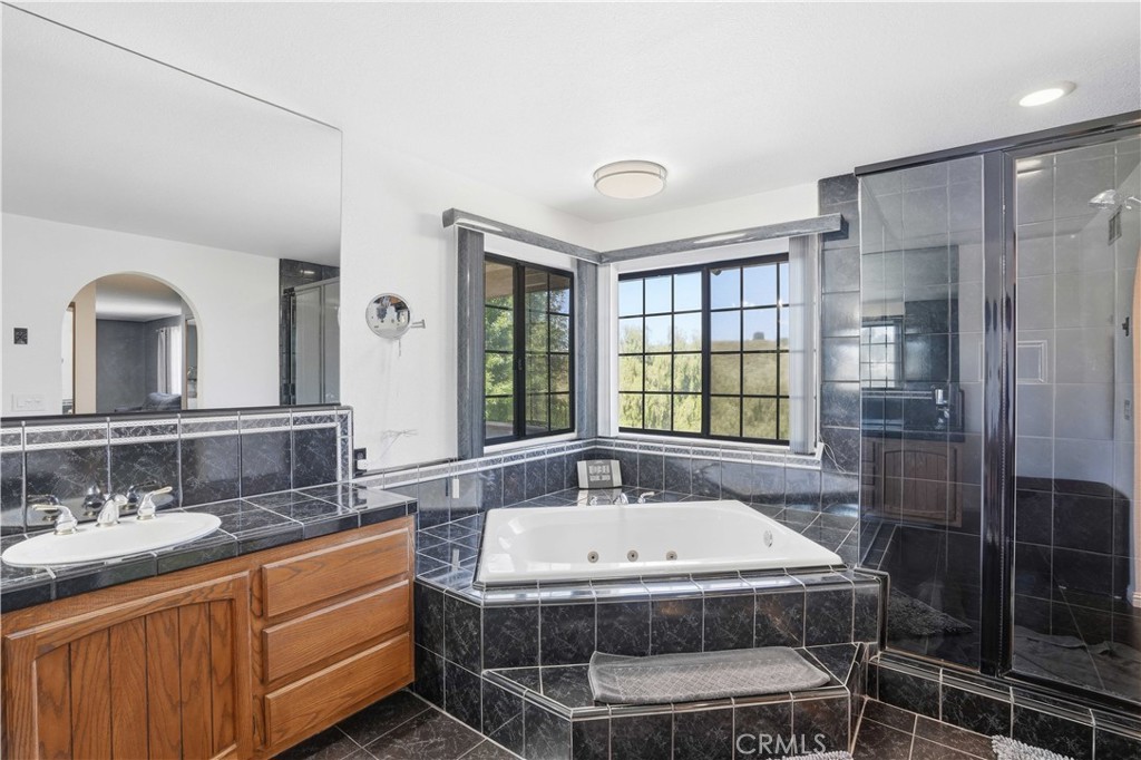 Bathroom with a built-in soaking tub beneath large windows, dark tile, and a glass-enclosed shower.