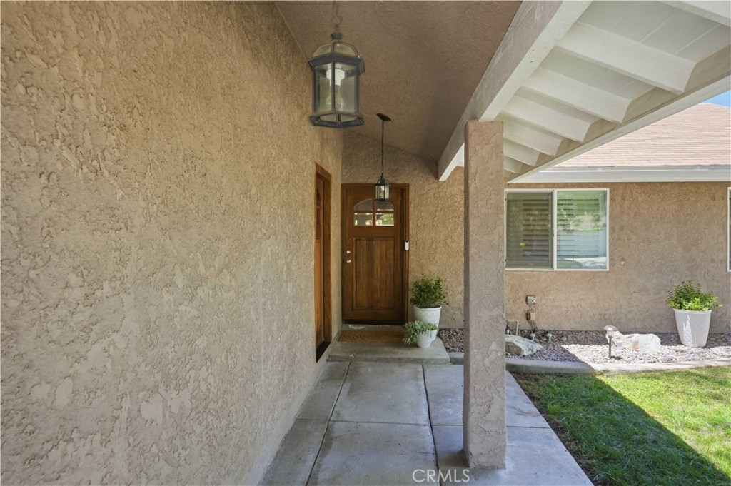 Covered home entry with a wooden front door, stucco walls, and potted plants.