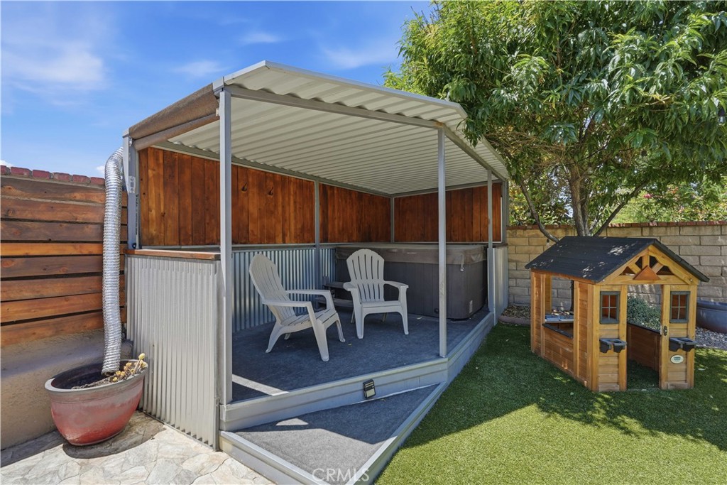 Covered backyard hot tub area with two chairs beside a wooden playhouse.