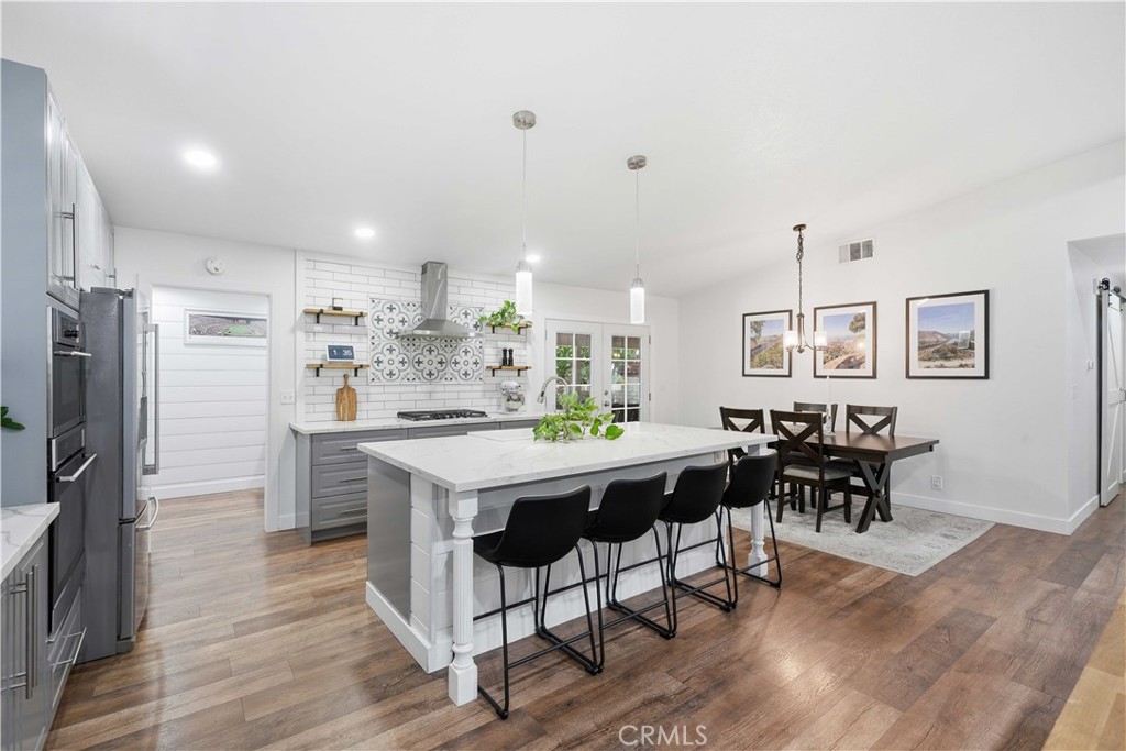 Kitchen with a large white island, black bar stools, patterned tile backsplash, and adjoining dining area.