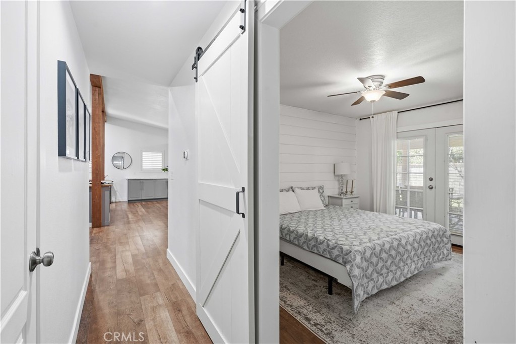 Furnished bedroom with a patterned bedspread and glass doors, viewed from a wood-floored hallway.