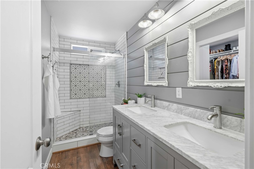 Bathroom with a double-sink gray vanity and a glass-enclosed subway-tile shower.