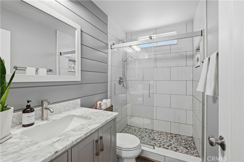 Bathroom with a marble-look vanity and glass shower featuring white tile and a pebble floor.