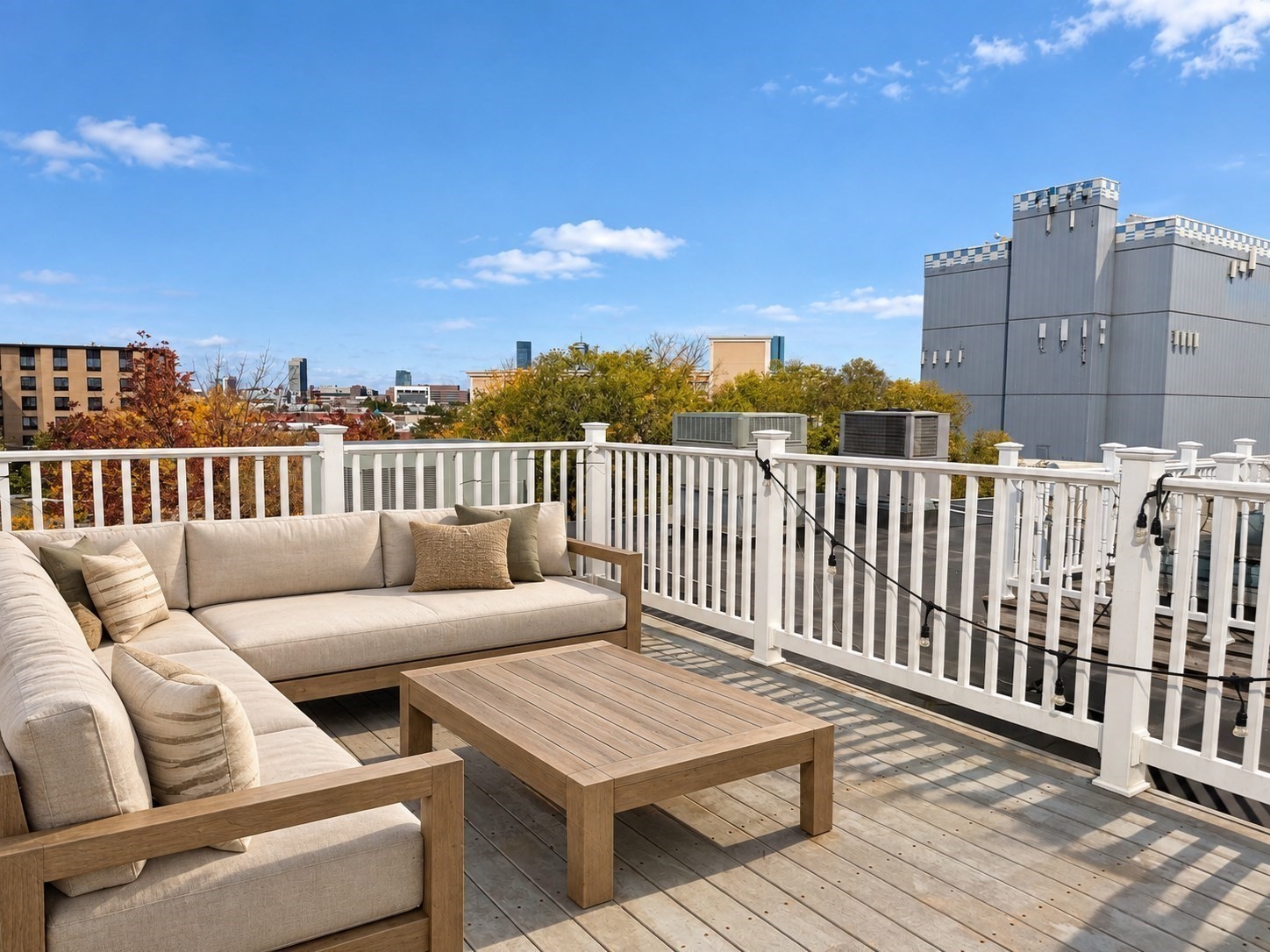 Furnished rooftop deck with beige sectional seating, wood flooring, and nearby city buildings.