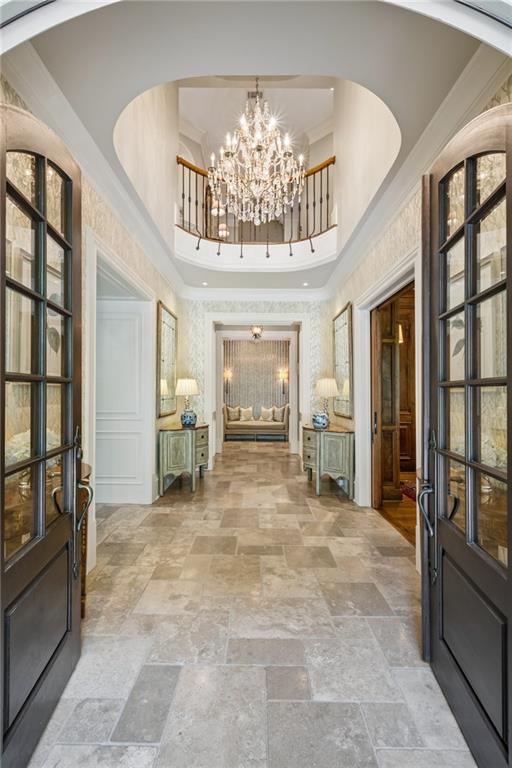 Grand entry foyer with stone floors, a crystal chandelier, and an upper-level curved balcony.