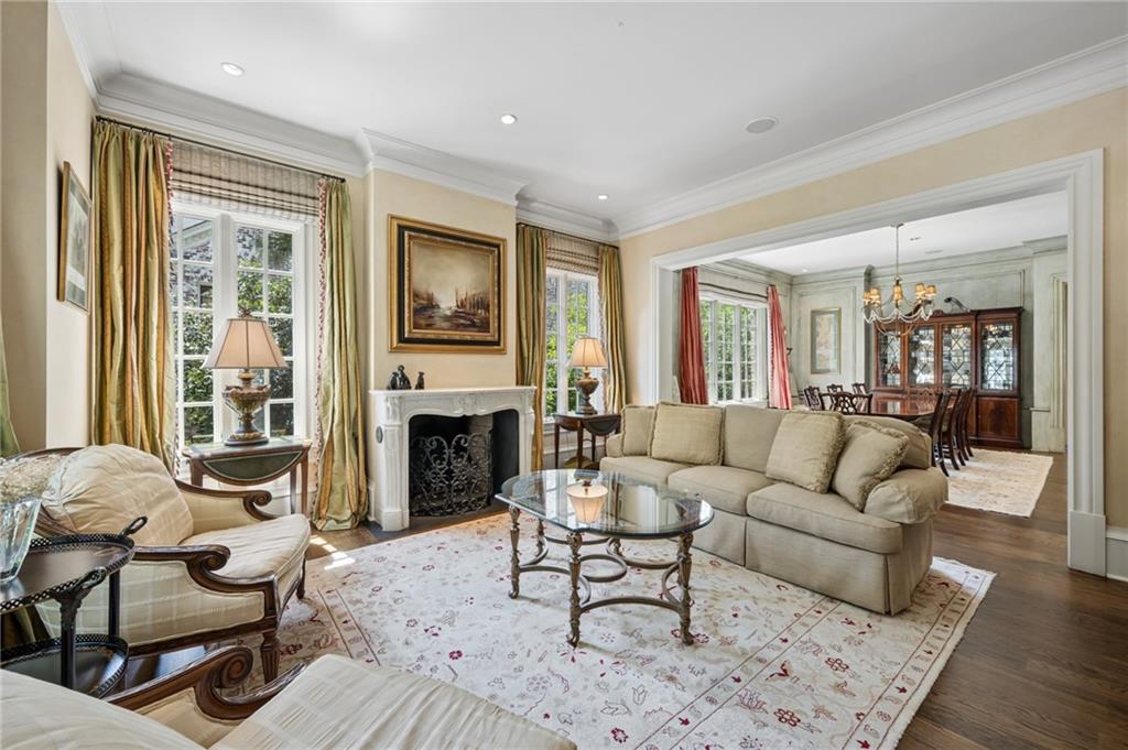 Living room with a white fireplace, cream seating, tall windows, and an adjoining dining room.