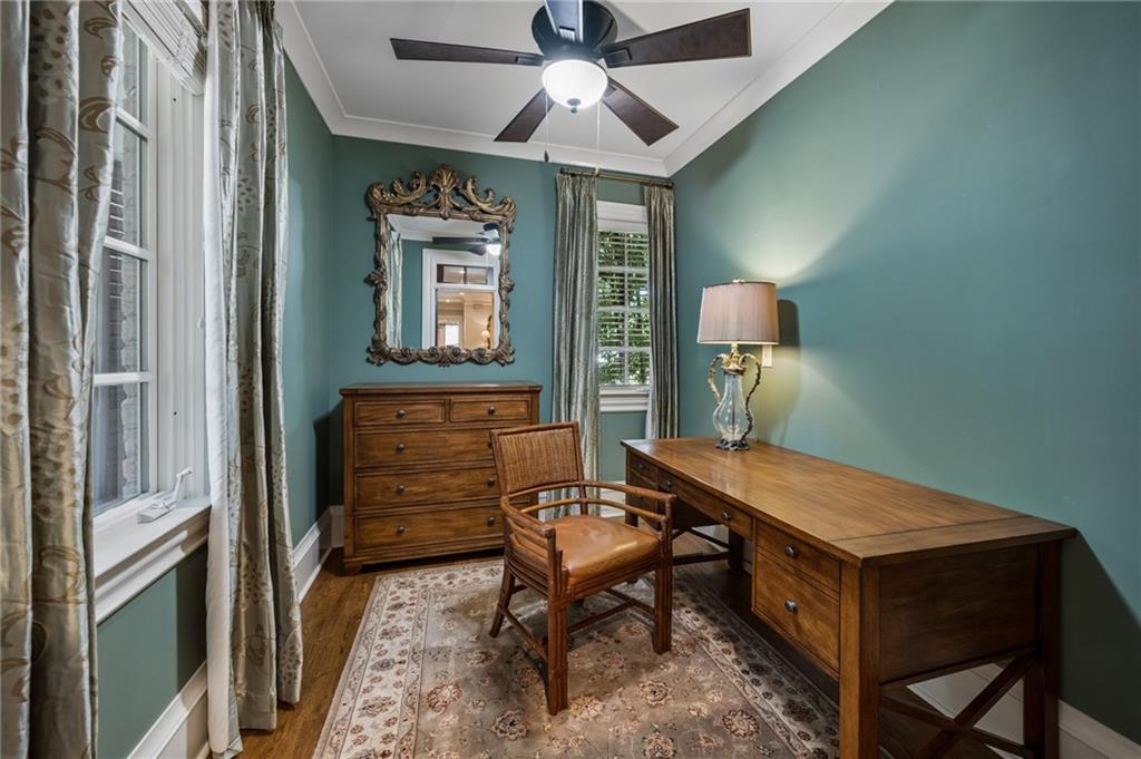 Teal home office with a wooden desk, leather chair, and tall curtained windows.