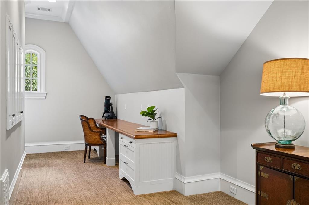 Attic office nook with a wooden desk, white drawers, wicker chair, and arched window.