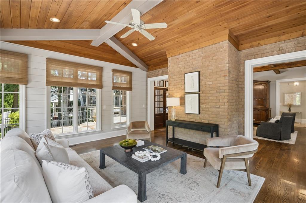 Staged living room with a vaulted wood ceiling, brick accent wall, and large windows.