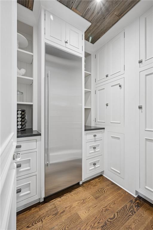 Kitchen pantry with a stainless steel refrigerator, white built-in cabinetry, open shelves, and a wood-plank ceiling.