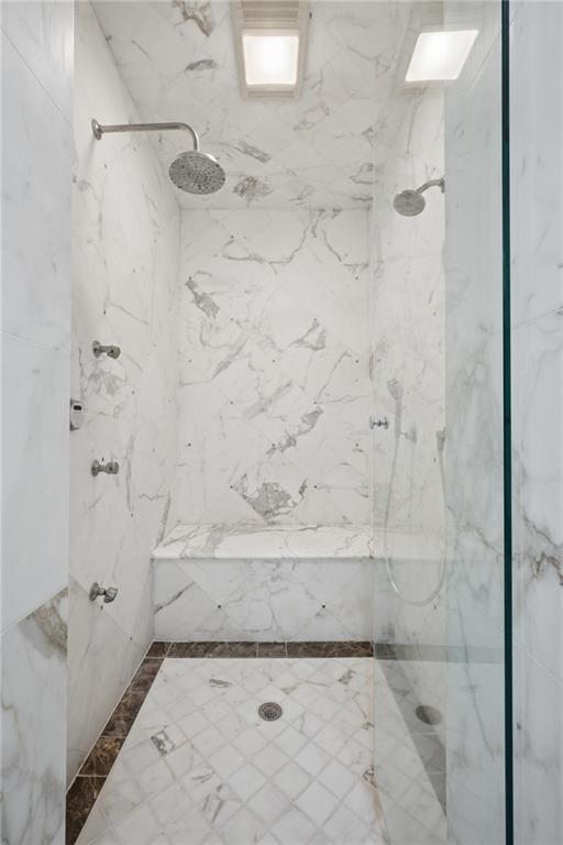 Marble-tiled walk-in shower with dual showerheads, built-in bench, and glass enclosure.