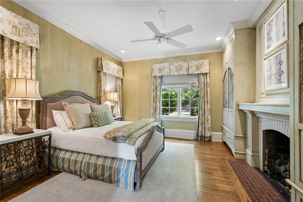 Bedroom with a large bed, patterned curtains, hardwood floors, and a fireplace.
