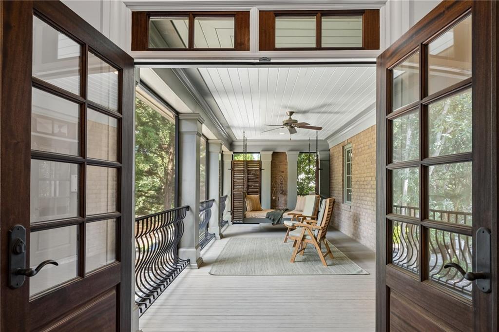 Covered porch with brick wall, black railing, and seating viewed through open French doors.