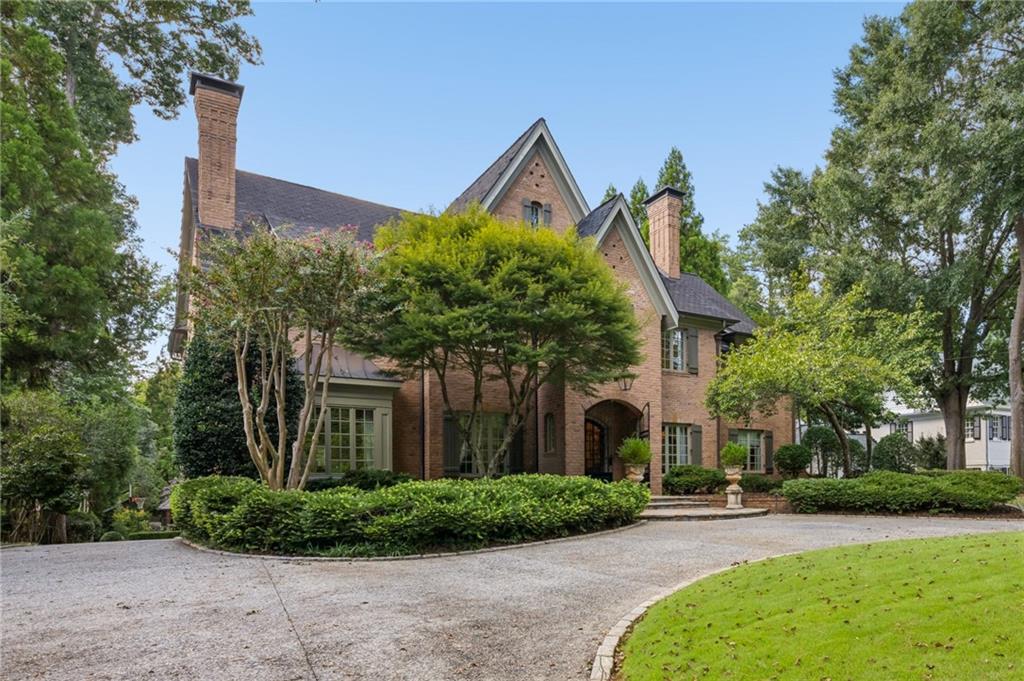 Brick house with steep gables, an arched entrance, mature trees, and a curved driveway.