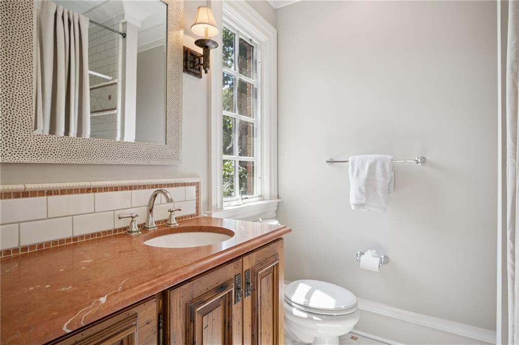Bathroom with a wood vanity and stone countertop beside a window and toilet.