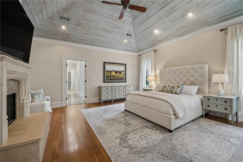 Bedroom with a vaulted white plank ceiling, upholstered bed, and stone fireplace.