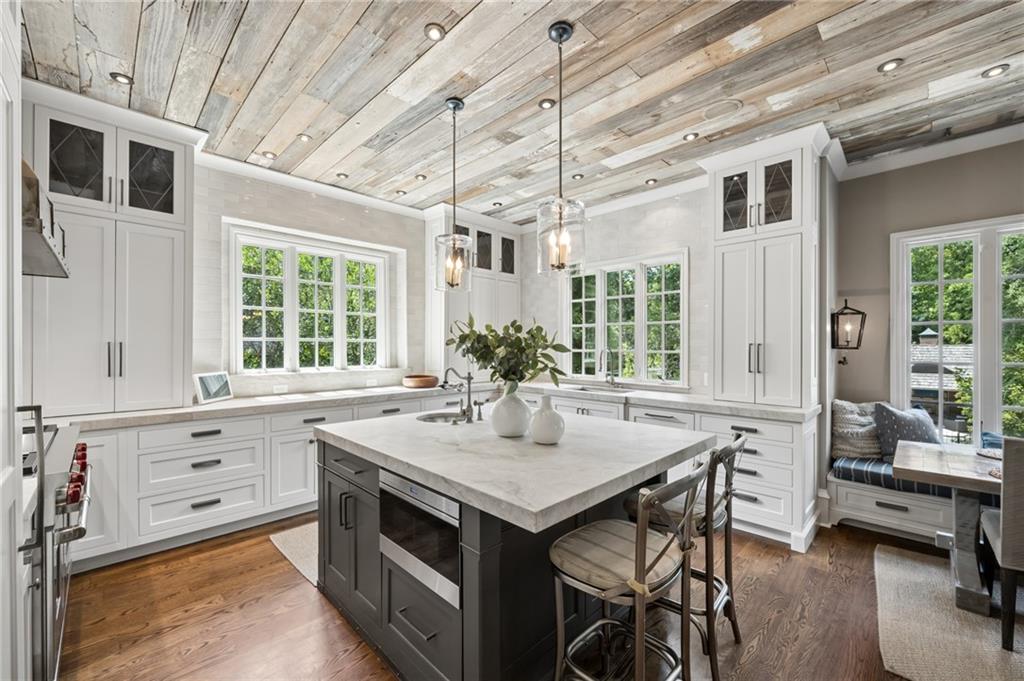 Bright kitchen with a dark island, white cabinets, pendant lights, and a weathered wood ceiling.
