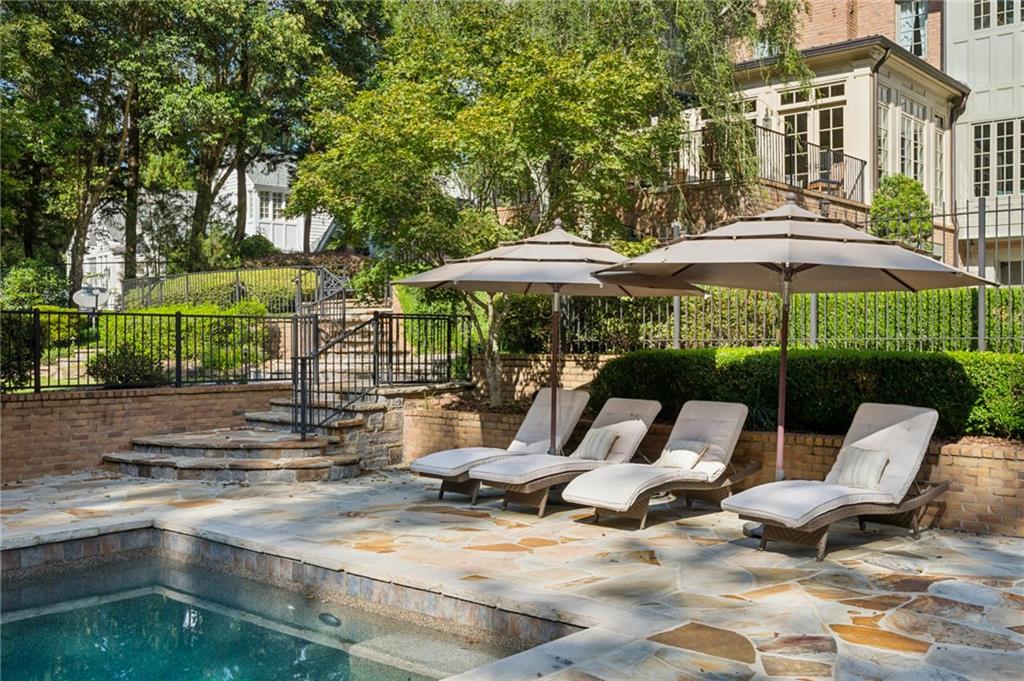 Outdoor swimming pool with stone patio, cushioned loungers, and large shade umbrellas.
