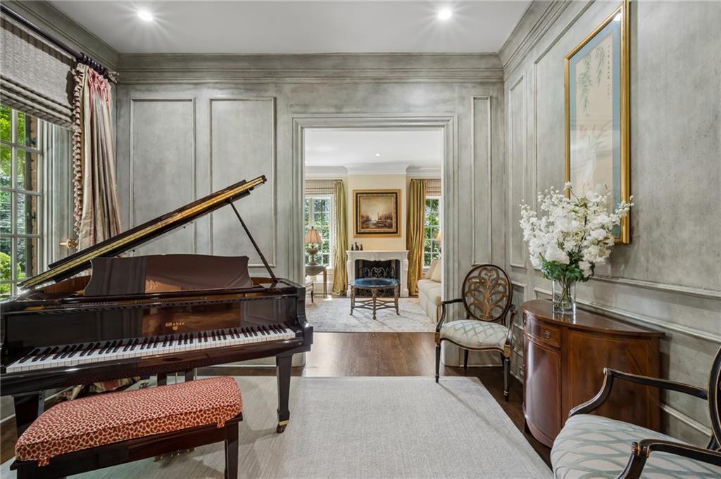 Music room with a black grand piano, paneled gray walls, and a view into the living room.