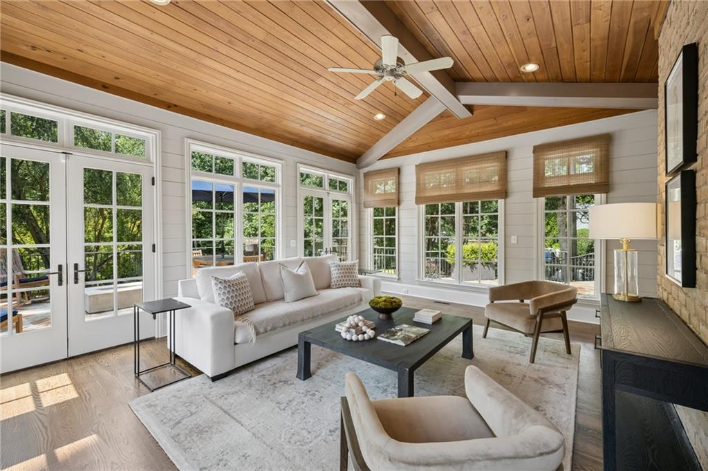 Living room with a vaulted wood ceiling, white sofas, and large windows overlooking greenery.