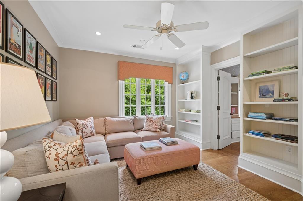 Living room with a beige sectional, coral ottoman, built-in bookshelves, and a leafy view.