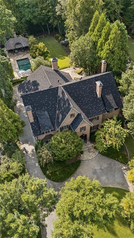 Aerial view of a brick house with a pool, detached pavilion, and mature trees.
