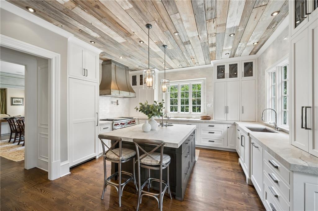 Bright white kitchen with a gray island, four stools, and a whitewashed plank ceiling.