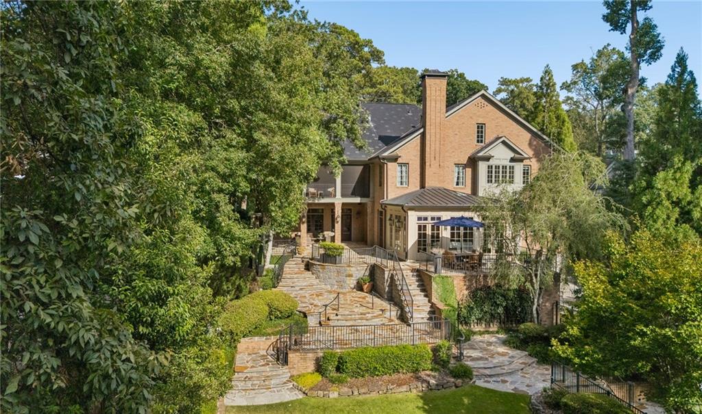Brick home with a tall chimney above terraced stone patios and landscaped gardens.