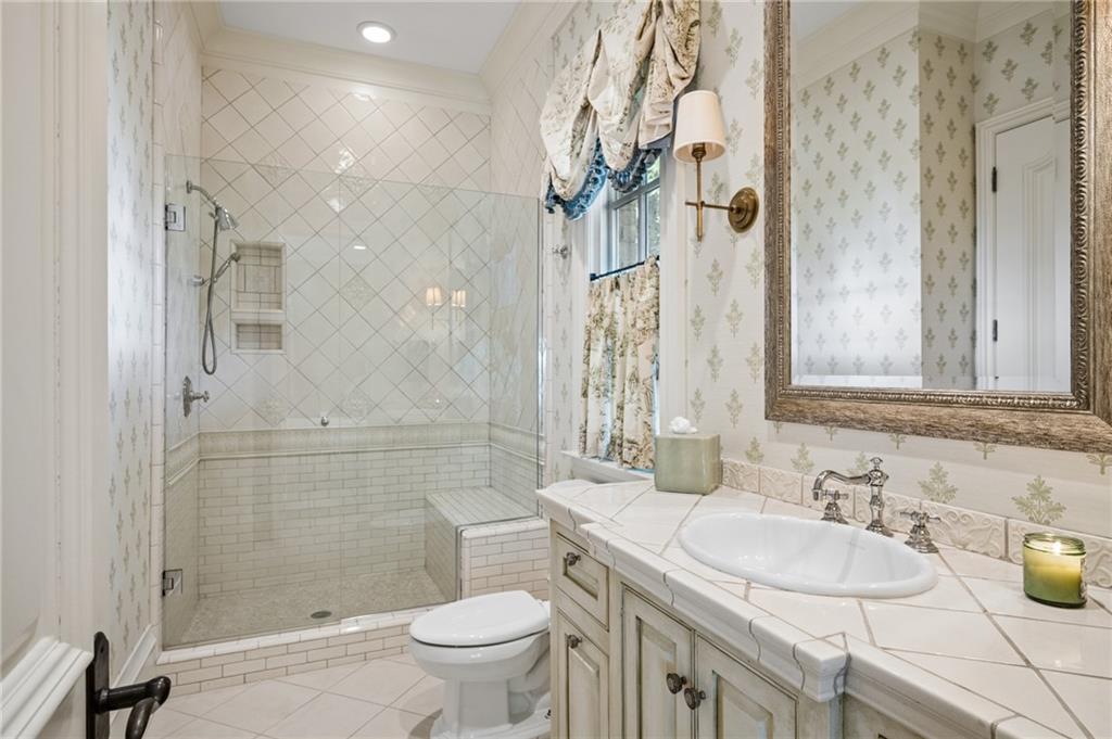 Traditional bathroom with a glass walk-in shower, tiled bench, and long vanity beneath an ornate mirror.