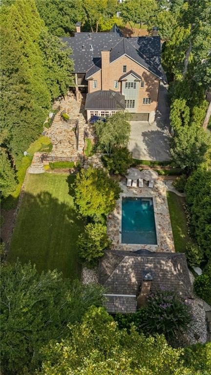 Aerial view of a brick home with a stone patio and rectangular pool amid mature trees.