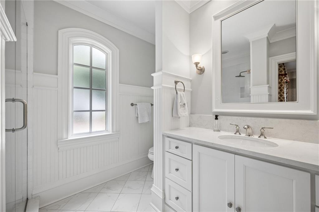 Bathroom with a white marble-top vanity, large mirror, arched window, and glass shower.