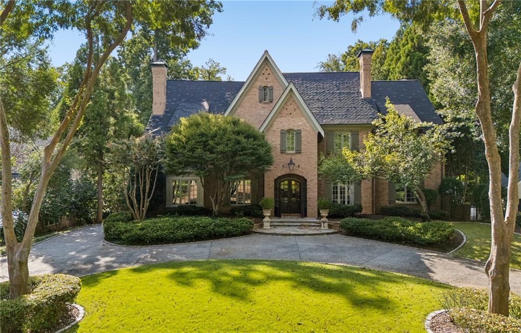 Two-story brick house with a curved driveway, landscaped lawn, and mature trees.