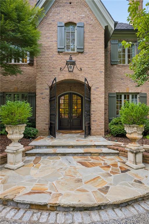 Brick home entrance with arched double doors, stone steps, and matching urn planters.