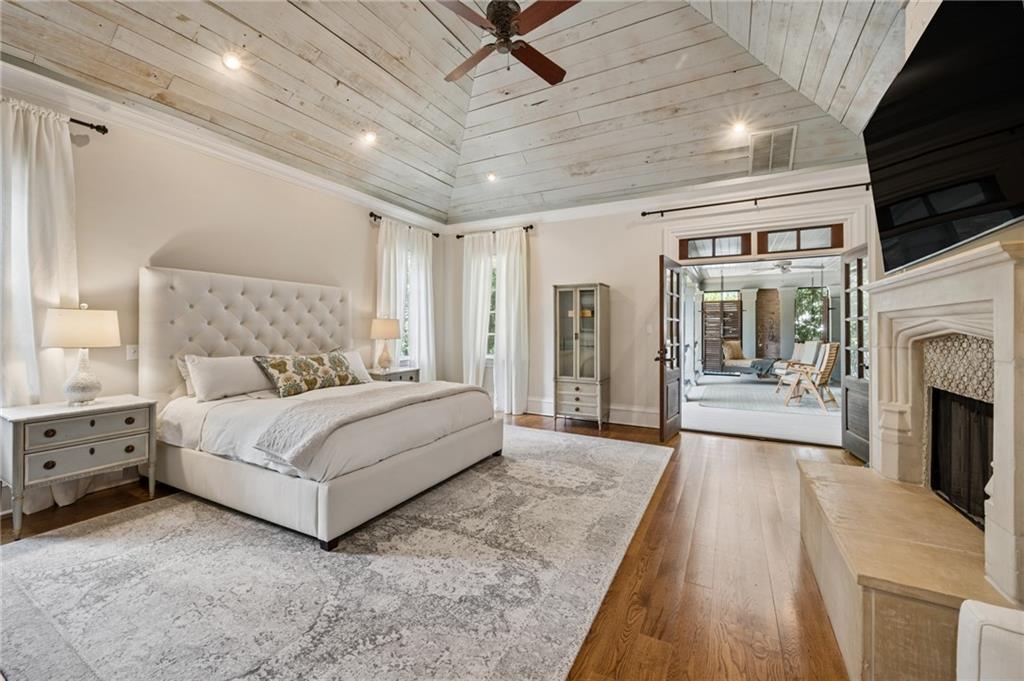 Bedroom with a tufted bed beneath a white vaulted plank ceiling, opening onto a sitting area.