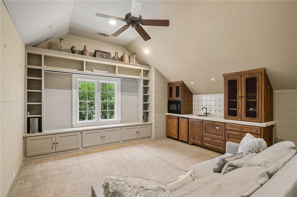 Living room with built-in shelving, a window seat, and a kitchenette with wood cabinets.