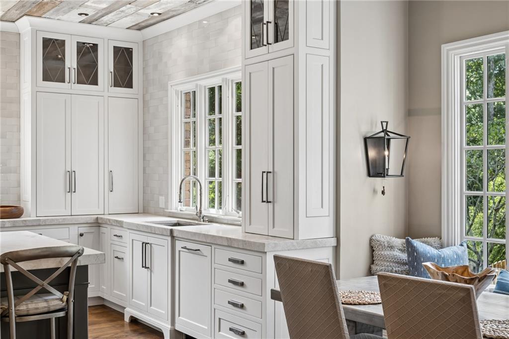 Bright white kitchen with a farmhouse sink beneath large windows and an adjoining dining area.