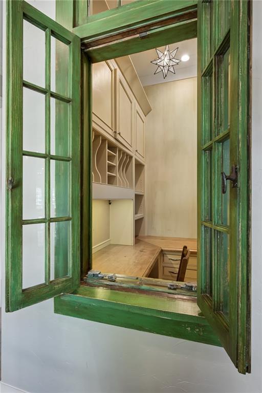 Built-in office nook with a wooden desk and shelves, viewed through a weathered green-framed window.