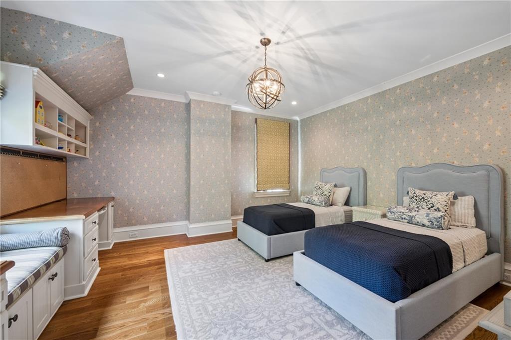 Bedroom with two upholstered twin beds, patterned wallpaper, hardwood floors, and built-in cabinetry.