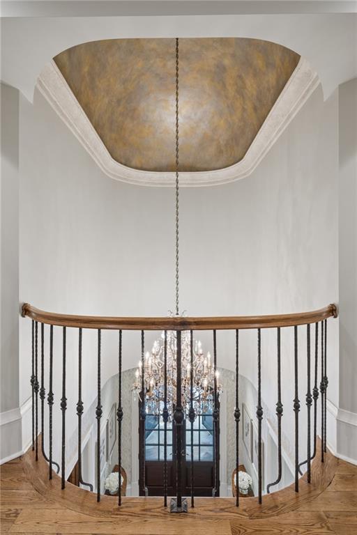 Upper-level foyer landing with curved iron railing, chandelier, double doors, and painted ceiling.