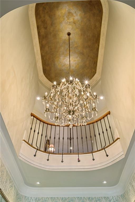 Grand foyer with a crystal chandelier beneath a curved balcony and decorative ceiling.