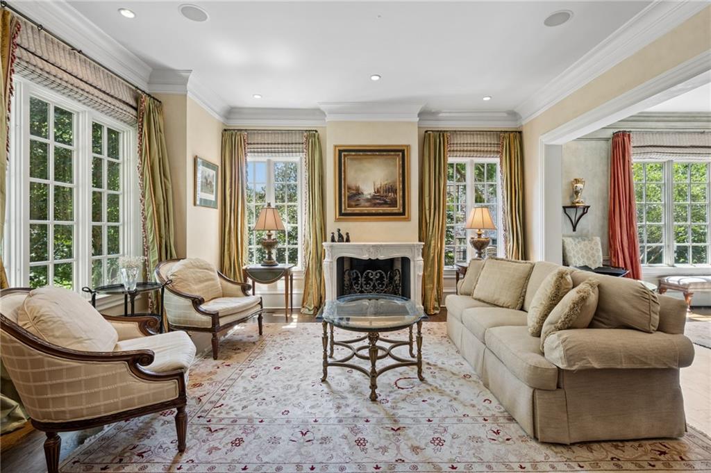 Living room with a fireplace, beige seating, tall windows, and a patterned rug.