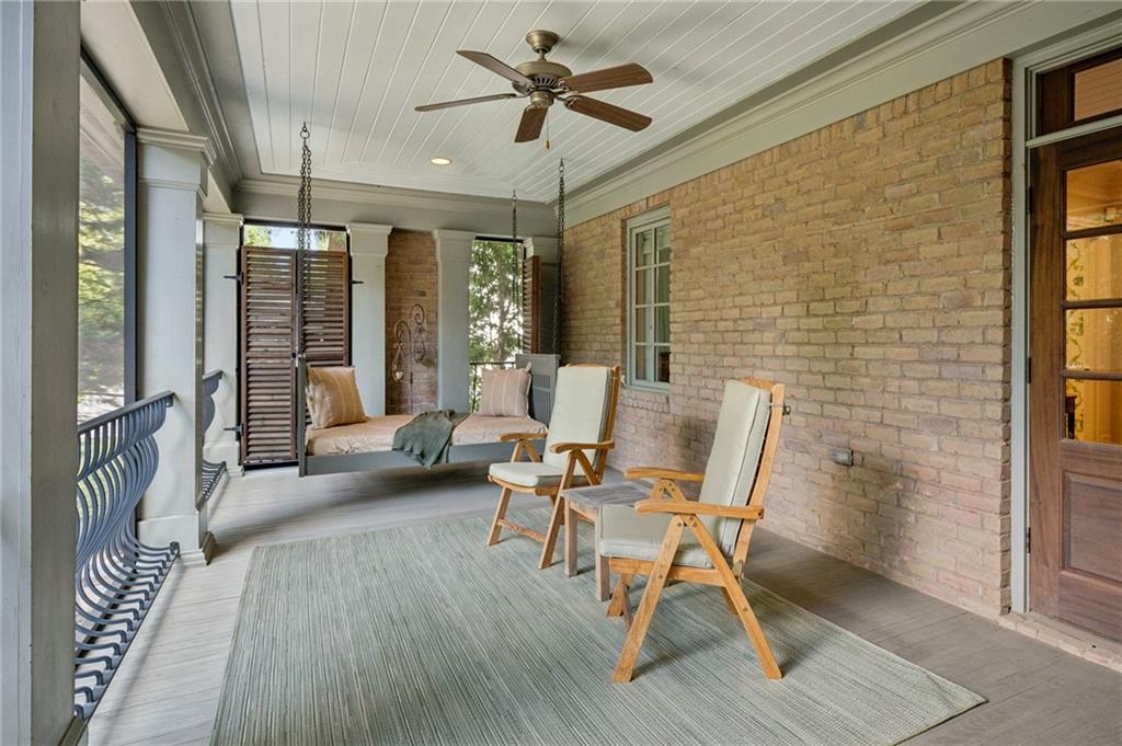 Covered porch with a brick wall, ceiling fan, wooden lounge chairs, and a daybed.