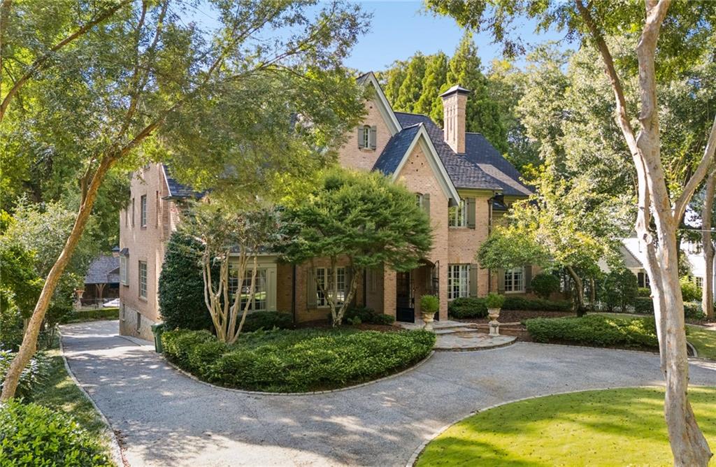 Two-story brick house with steep roofs, mature trees, and a curved driveway.