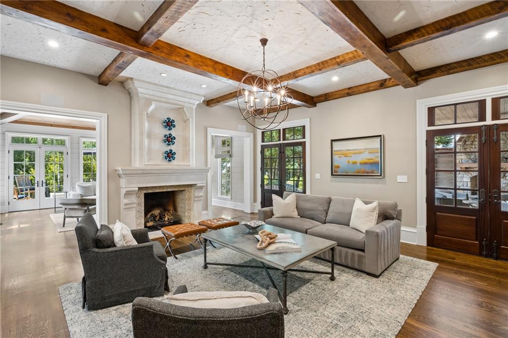 Living room with a stone fireplace, exposed wood beams, and gray seating around a coffee table.
