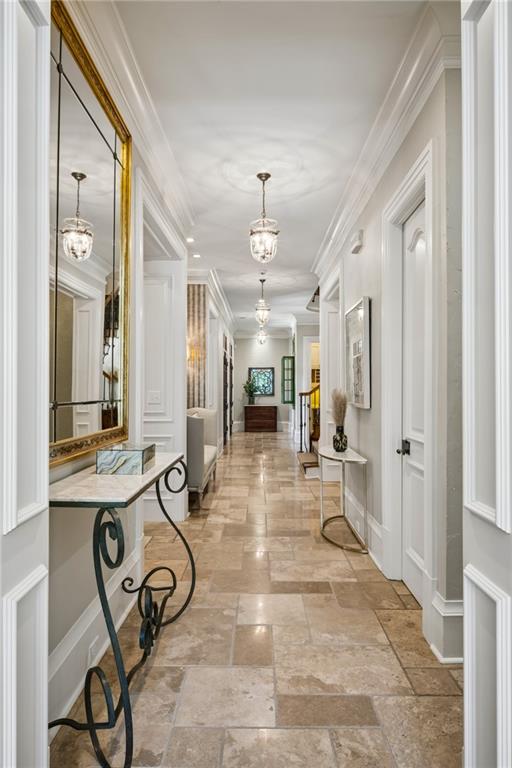 Elegant hallway with stone tile floors, white paneled walls, and a gold-framed mirror.